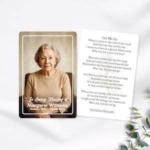 May include: A memorial card with a portrait of an elderly woman in a tan sweater. The card reads "In Loving Memory of Margaret Williams, January 1952 - March 2025." Beside it is a card with the poem "Let Me Go" by Christina Rossetti.