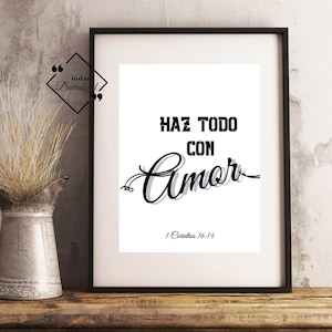 May include: A framed print with the words "HAZ TODO CON Amor" in black, with the scripture reference 1 Corinthians 16:14. The print is in a black frame and is displayed on a wooden surface.