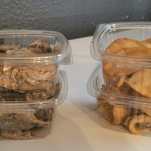 Könnte beinhalten: Zwei Stapel klarer Plastikbehälter, die jeweils eine andere Art von Lebensmitteln enthalten. Ein Stapel enthält getrockneten Fisch, der andere gebratene, goldbraune Lebensmittel, möglicherweise Chips oder Snacks. Die Behälter stehen auf einer weißen Oberfläche.