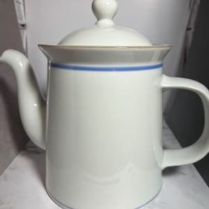 May include: A white ceramic teapot with a lid and handle. The teapot has a blue stripe around the middle and a gold trim. The spout is curved, and the handle is a simple loop.