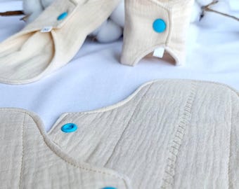 Puede incluir: Tres compresas de tela reutilizables con botones a presión azules. Las compresas están hechas de una tela suave y natural y están diseñadas para la higiene menstrual.