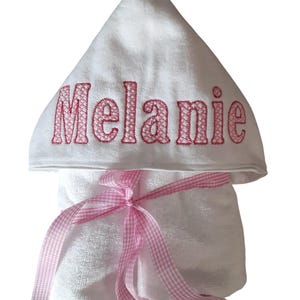 May include: White hooded towel with a pink gingham ribbon tied around it. The hood has the name "Melanie" embroidered in pink.
