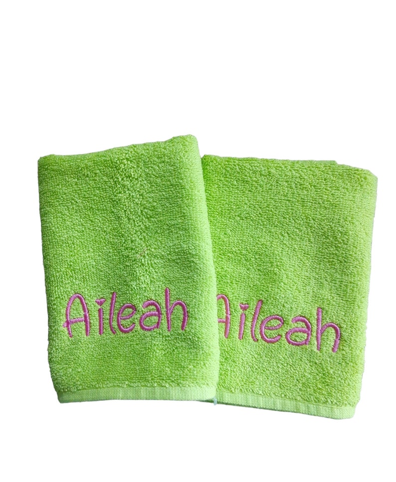 May include: Two lime green terry cloth hand towels, each featuring the name Aileah embroidered in a bright pink cursive font. The towels have a textured, absorbent surface and are positioned side by side against a plain white background.
