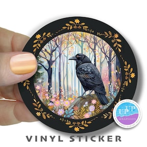 May include: A round vinyl sticker with a black background and a gold frame. The sticker features a detailed illustration of a crow perched on a branch in a forest setting. The forest is filled with colorful flowers and trees. The sticker has the text "UPP GRAPHICS" in a purple circle with a gold border.