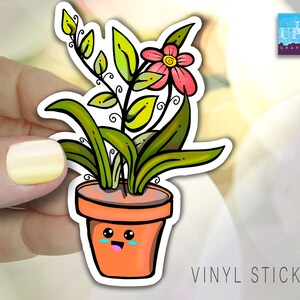 May include: A vinyl sticker featuring a cartoon illustration of a potted plant with a pink flower and a smiling face. The plant has green leaves and is in a brown pot. The sticker says "VINYL STICKER" at the bottom.