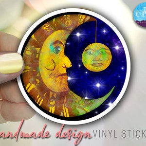 May include: A round vinyl sticker with a colorful illustration of a sun and moon. The sun is yellow and orange with a human face. The moon is a crescent shape with a blue and green background and a human face. The sticker has a white border.