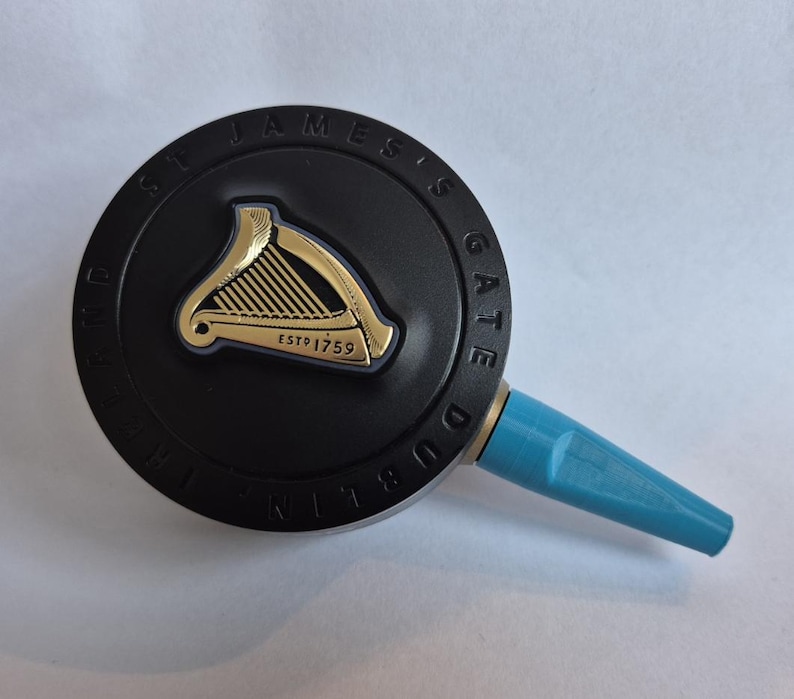 K&ouml;nnte beinhalten: Ein schwarzer Zapfhahn mit einem goldenen Harfenemblem und dem Text "ST JAMES'S GATE DUBLIN". Der Griff hat einen hellblauen Ausguss. Das Emblem ist auf einer kreisf&ouml;rmigen schwarzen Basis gepr&auml;gt.