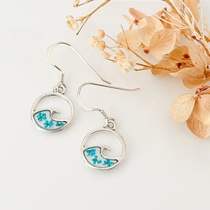 May include: Silver earrings with a wave design and blue pressed flowers inside the circle.