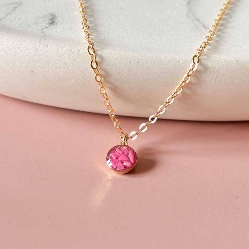 May include: A gold chain necklace with a small round pendant filled with pink confetti.