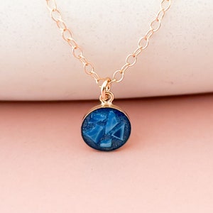 May include: A gold chain necklace with a small round pendant featuring a blue resin design with geometric shapes.