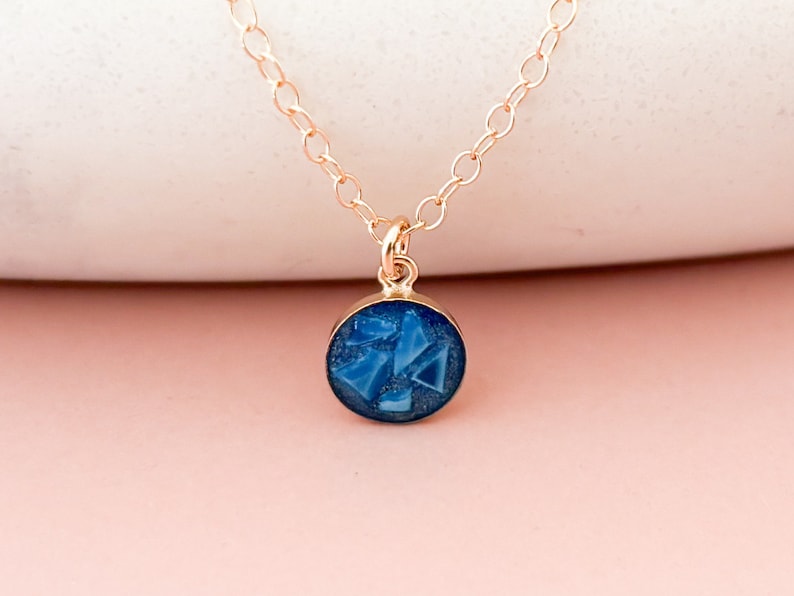 May include: A gold chain necklace with a small round pendant featuring a blue resin design with geometric shapes.
