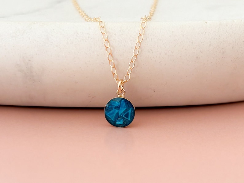 May include: A gold chain necklace with a round pendant featuring a blue geometric design.