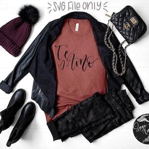 May include: A flat lay of a fashion ensemble featuring a rust-coloured t-shirt with the words "Te Amo" and a heart, a black leather jacket, black jeans, black boots, a burgundy knit hat with a black pom-pom, and a black quilted purse.