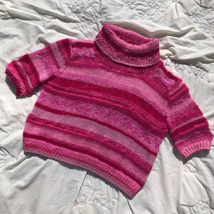 Op de afbeelding: Een roze gestreepte trui met een rolkraag en een pluche textuur.
