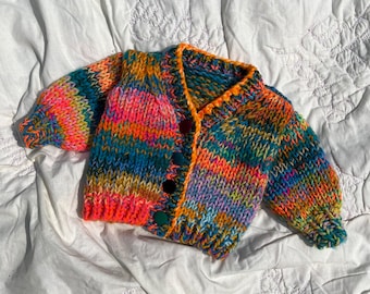 May include: A colorful striped knitted cardigan with a button closure. The cardigan is made with a variety of bright colors, including pink, orange, green, blue, and purple.