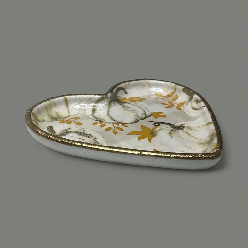 Pu&ograve; includere: Piatto in ceramica a forma di cuore con base bianca, bordo dorato e design a zucca e foglie. Decorato con zucche bianche e foglie gialle, perfetto per l'arredamento autunnale.