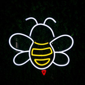 Puede incluir: Luz de ne&oacute;n blanca con forma de abeja con rayas amarillas y negras. La abeja est&aacute; delineada en blanco y tiene un coraz&oacute;n rojo en la parte inferior.