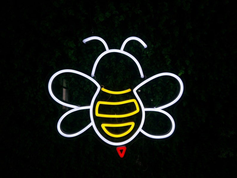 Puede incluir: Luz de ne&oacute;n blanca con forma de abeja con rayas amarillas y negras. La abeja est&aacute; delineada en blanco y tiene un coraz&oacute;n rojo en la parte inferior.