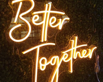 May include: A neon sign with the words "Better Together" in a white script font on a clear background. The sign is illuminated with a warm yellow glow.