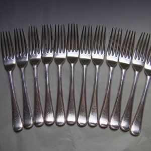 May include: A set of 12 silver forks with ornate handles. The forks are arranged in a row on a grey surface.
