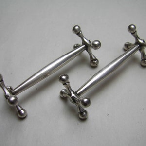 May include: A pair of silver knife rests with a unique, geometric design. Each rest features a central rod with five ball-shaped ends.