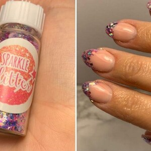 May include: A close-up of a hand with nails painted with a light pink polish and decorated with iridescent glitter. The glitter is in a small jar labelled "Sparkle Glitter".