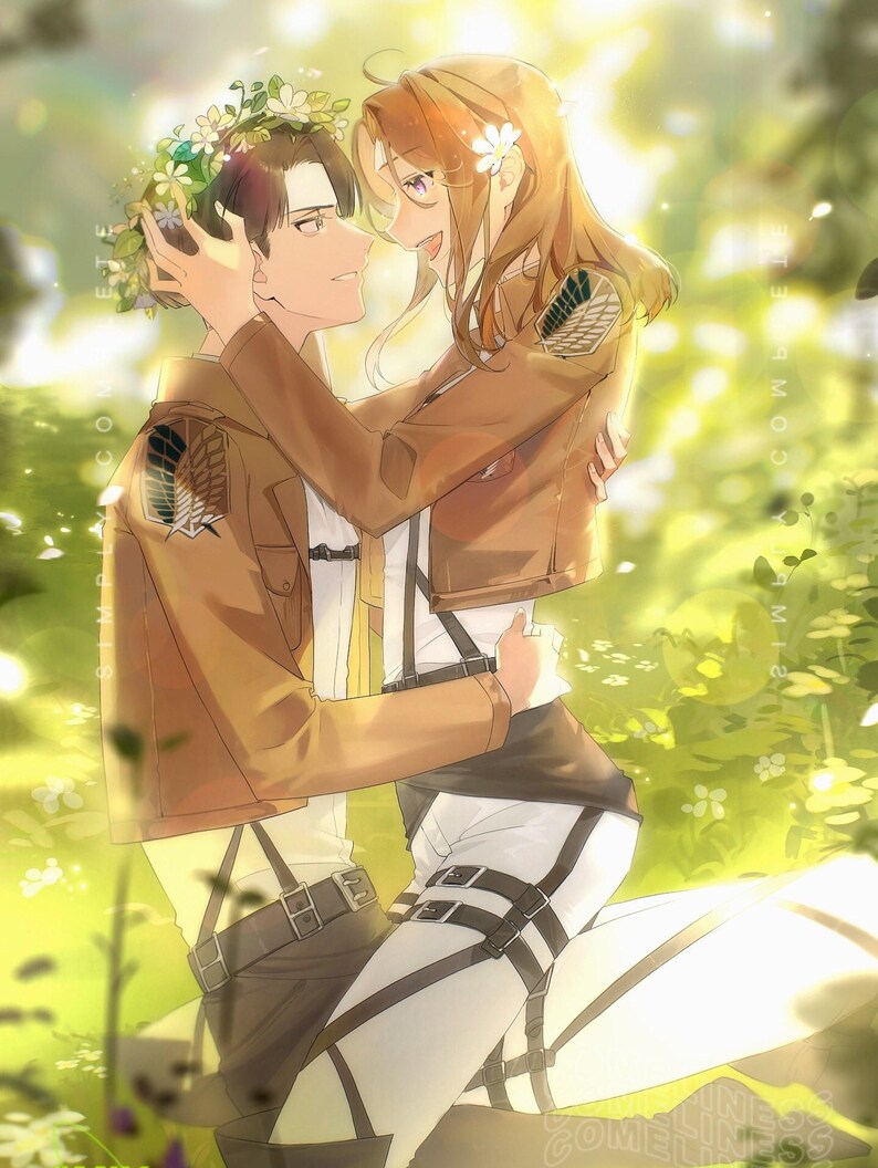 May include: A couple in a woodland setting, the woman is wearing a flower crown and holding the man's face. They are both wearing brown jackets with the same emblem on the back. The background is a blurred image of green trees and flowers.