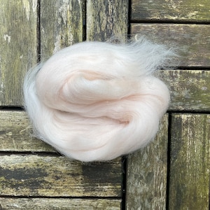 May include: A close-up of a light pink ball of wool fiber. The wool is soft and fluffy, and it is perfect for knitting or crocheting.