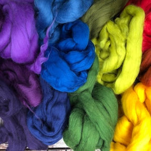 May include: A collection of colorful wool roving in shades of purple, blue, green, yellow, orange, and red. The wool is arranged in a circular pattern, with the different colors overlapping.