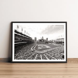 Może przedstawiać: Czarno-białe zdjęcie stadionu baseballowego, Progressive Field, z dużym tłumem ludzi na trybunach. Pole jest puste, widoczne są bazy i kopiec miotacza.