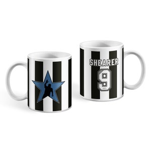 Puede incluir: Dos tazas de cer&aacute;mica blanca con rayas blancas y negras. Una taza presenta una estrella azul con la silueta de un jugador de f&uacute;tbol. La otra taza tiene el texto "SHEARER" y el n&uacute;mero "9" en negro.