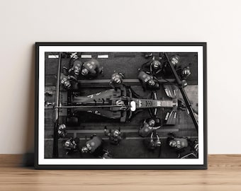 May include: Black and white framed print of a Formula 1 race car in a pit stop. The image shows the car surrounded by crew members, with a focus on the vehicle's details and the team's activity. The print is displayed on a wooden surface.