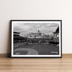 May include: A black and white photograph of a baseball stadium, T-Mobile Park in Seattle, with a crowd of people in the stands and the city skyline in the background.