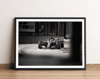 Könnte beinhalten: Schwarz-Weiß-Druck eines Formel-1-Rennwagens, der eine Kurve nimmt. Das Bild zeigt das Auto in Bewegung, mit verschwommenem Hintergrund, um die Geschwindigkeit zu betonen. Der Druck wird auf einer Holzoberfläche präsentiert.