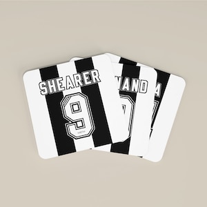 Könnte beinhalten: Vier schwarz-weiße Untersetzer mit den Namen "Shearer 9" und "Owen 7" darauf gedruckt. Die Untersetzer sind so gestaltet, dass sie einem Fußballtrikot ähneln.