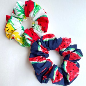 May include: Two fabric hair scrunchies. One is white with green and red watermelon print. The other is navy blue with red and green watermelon print.