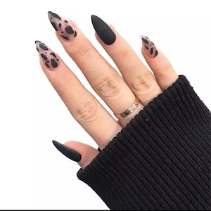 May include: A hand with black and white animal print nail polish on some fingers and solid black nail polish on others. The hand is wearing a gold ring.