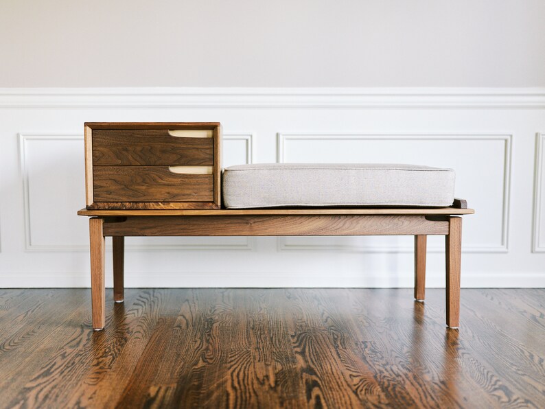 Pu&ograve; includere: Una panca in legno con un sedile imbottito e un'unit&agrave; a cassetti incorporata. La panca &egrave; realizzata in legno scuro con una finitura in legno chiaro. L'unit&agrave; a cassetti ha due cassetti con maniglie in legno chiaro.