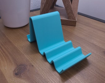 May include: A teal blue 3D printed phone stand with a wavy design. The stand is made of plastic and has a smooth finish.