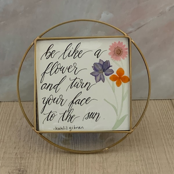 Round gold-rimmed frame with glass. Handwritten quote with pressed dried flowers.
