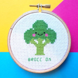 May include: A white embroidery hoop with a green broccoli design. The broccoli has a smiling face and the text "BROCC ON" is embroidered below it.
