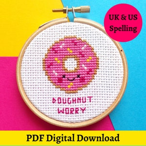 May include: A pink and brown donut with white sprinkles and a smiling face is stitched on white Aida cloth in a wooden embroidery hoop. The text "doughnut worry" is stitched below the donut. The text "UK & US Spelling" is in the upper right corner of the image. The text "PDF Digital Download" is at the bottom of the image.