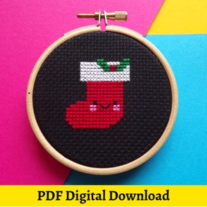 May include: A black and white cross stitch pattern of a red Christmas stocking with a white cuff and green holly on top. The stocking has a smiling face with pink cheeks. The pattern is framed in a wooden hoop.