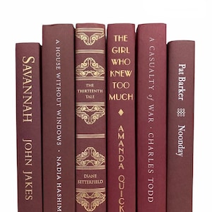 May include: A collection of seven hardcover books with burgundy covers and gold lettering. Titles include "Savannah," "A House Without Windows," "The Thirteenth Tale," "The Girl Who Knew Too Much," "A Casualty of War," and "Noonday."