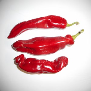 May include: Three red chili peppers on a white background. The peppers are long and slender, with a slightly curved shape.