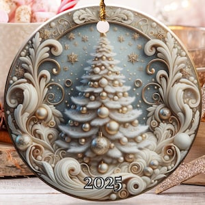 Puede incluir: Adorno navideño redondo con un diseño en relieve detallado que representa un árbol de Navidad y el año 2025. El adorno cuelga de un hilo dorado. Otras decoraciones navideñas están en el fondo.