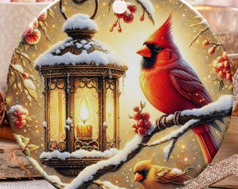 Peut inclure: Ornement de Noël rond avec un cardinal rouge sur une branche enneigée et une lanterne. L'ornement a une ficelle dorée pour l'accrocher. Autres décorations de vacances : cannes en sucre, étoile et sapin.