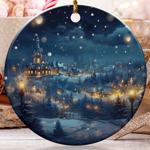 May include: A round Christmas ornament with a winter village scene in shades of blue and gold. The ornament hangs from a gold cord. The image includes a cup of marshmallows, candy canes, and other holiday decorations.