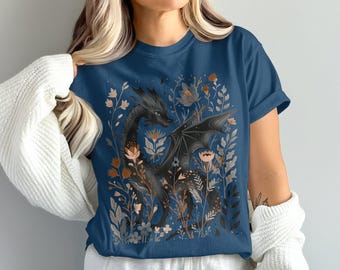 May include: A navy blue t-shirt featuring a black dragon illustration surrounded by flowers in shades of orange, beige, and gray. The dragon has detailed wings and is set against a floral background.