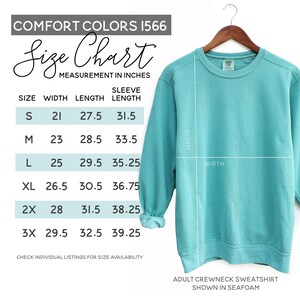May include: A seafoam green adult crewneck sweatshirt displayed on a wooden hanger. The image includes a size chart with measurements in inches for width, length, and sleeve length. The size chart includes sizes S, M, L, XL, 2X, and 3X.